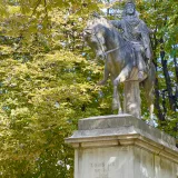Estatua ecuestre de Luis XIV rodeada de frondosa vegetación de parque.