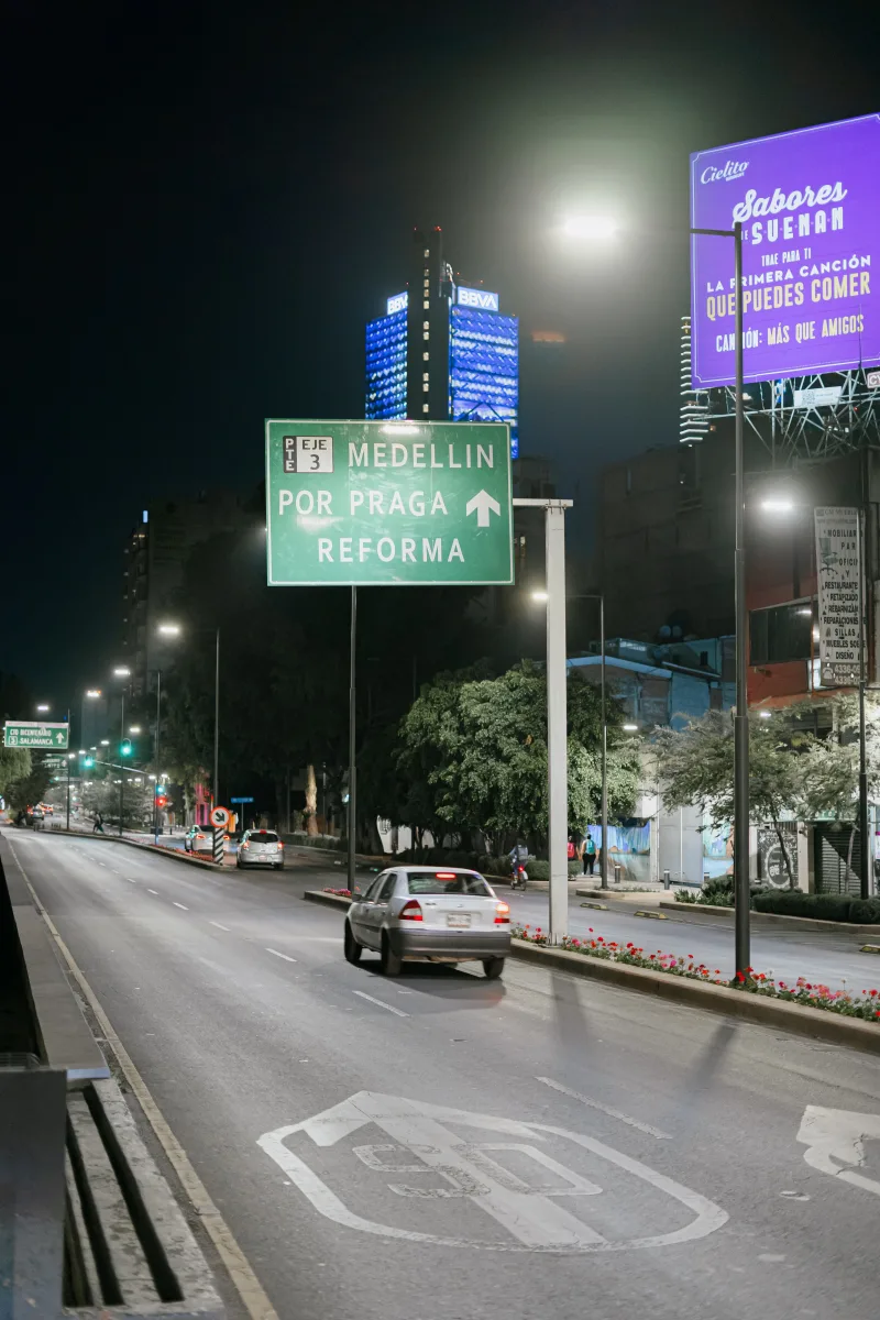 Urban night scene of a road in Ciudad de México, featuring street signs and a car.