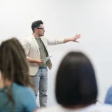 Un hombre con americana hace una presentación ante un público cautivado en un entorno de conferencias.