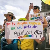 LGBTQ pride event with diverse crowd holding colorful signs and a powerful message of rebellion.