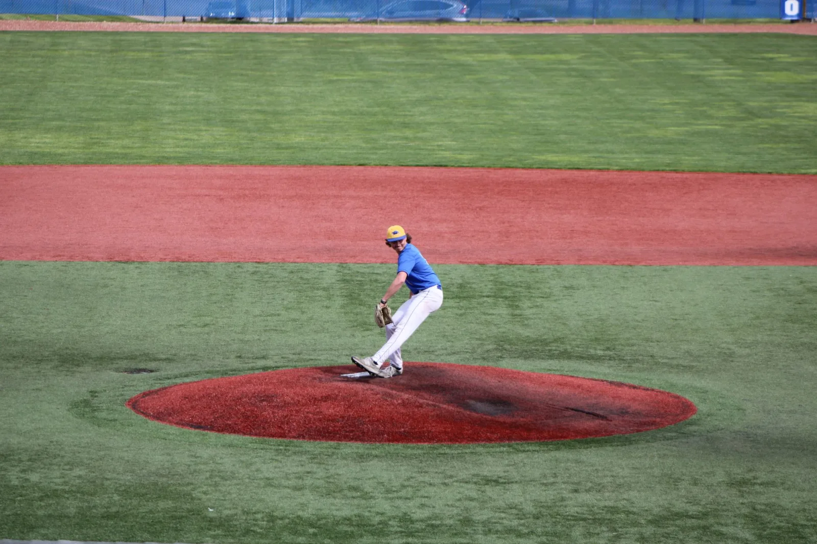 Lanzador de béisbol adolescente lanza una pelota en un campo al aire libre, demostrando habilidad atlética.
