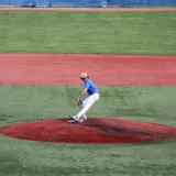Lanzador de béisbol adolescente lanza una pelota en un campo al aire libre, demostrando habilidad atlética.