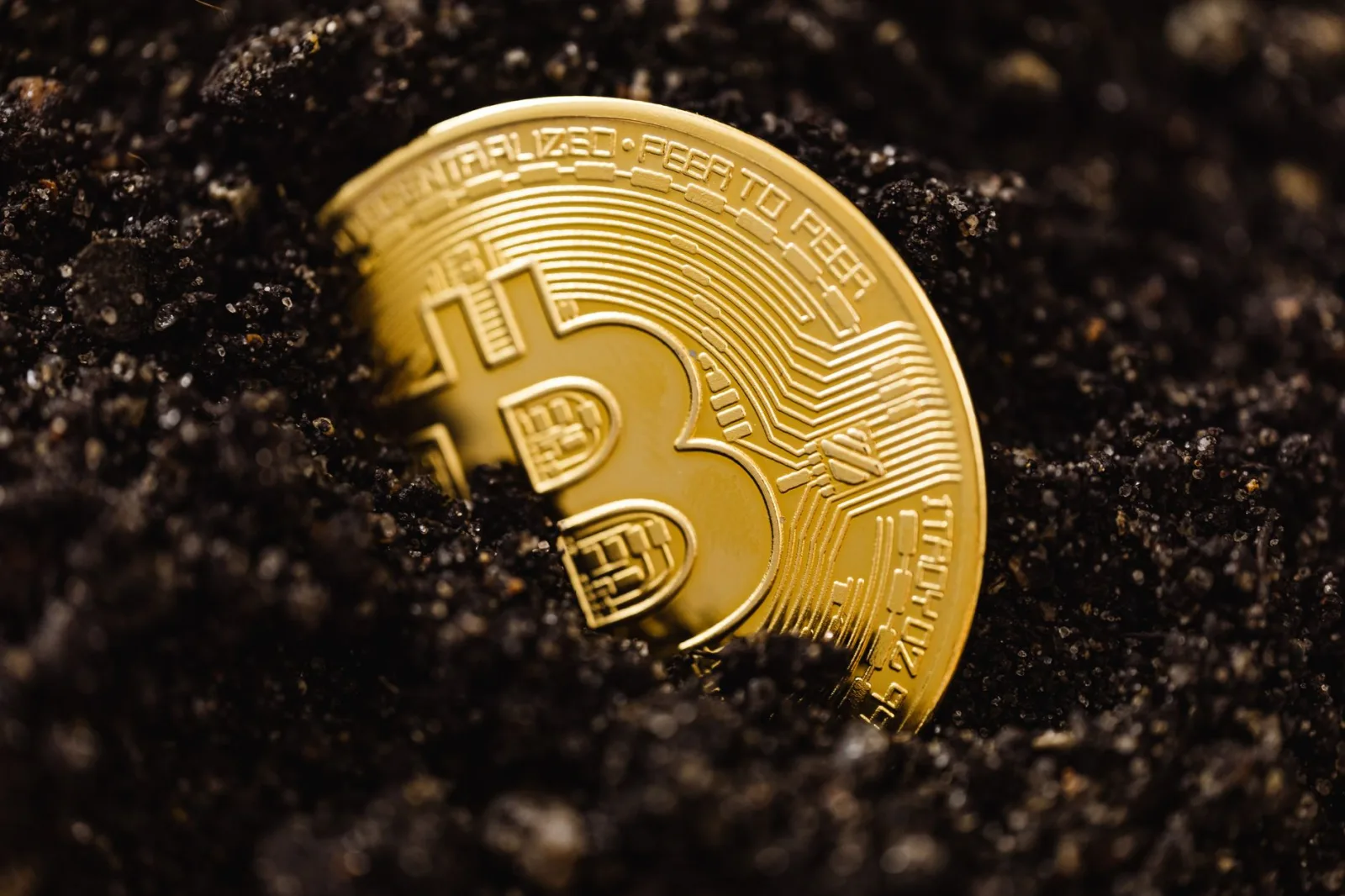 Bitcoin dorado parcialmente enterrado en suelo oscuro, simbolizando el crecimiento de la inversión.