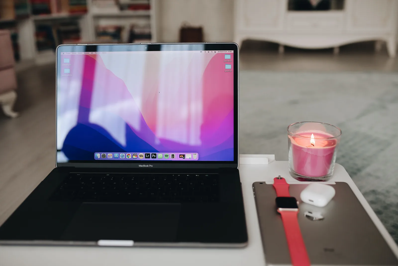 Un espacio de trabajo moderno con una computadora portátil, una vela, AirPods y un Apple Watch.