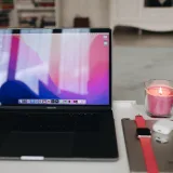 Un espacio de trabajo moderno con una computadora portátil, una vela, AirPods y un Apple Watch.