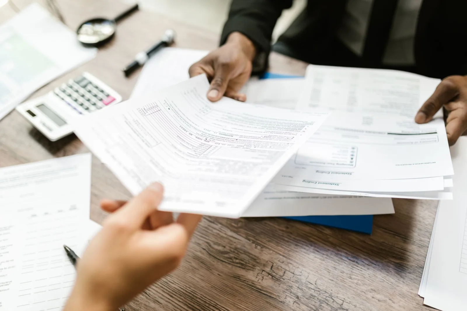 Dos profesionales intercambian documentos en una oficina, concentrados en el papeleo y el análisis de datos.