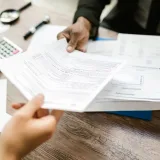 Dos profesionales intercambian documentos en una oficina, concentrados en el papeleo y el análisis de datos.