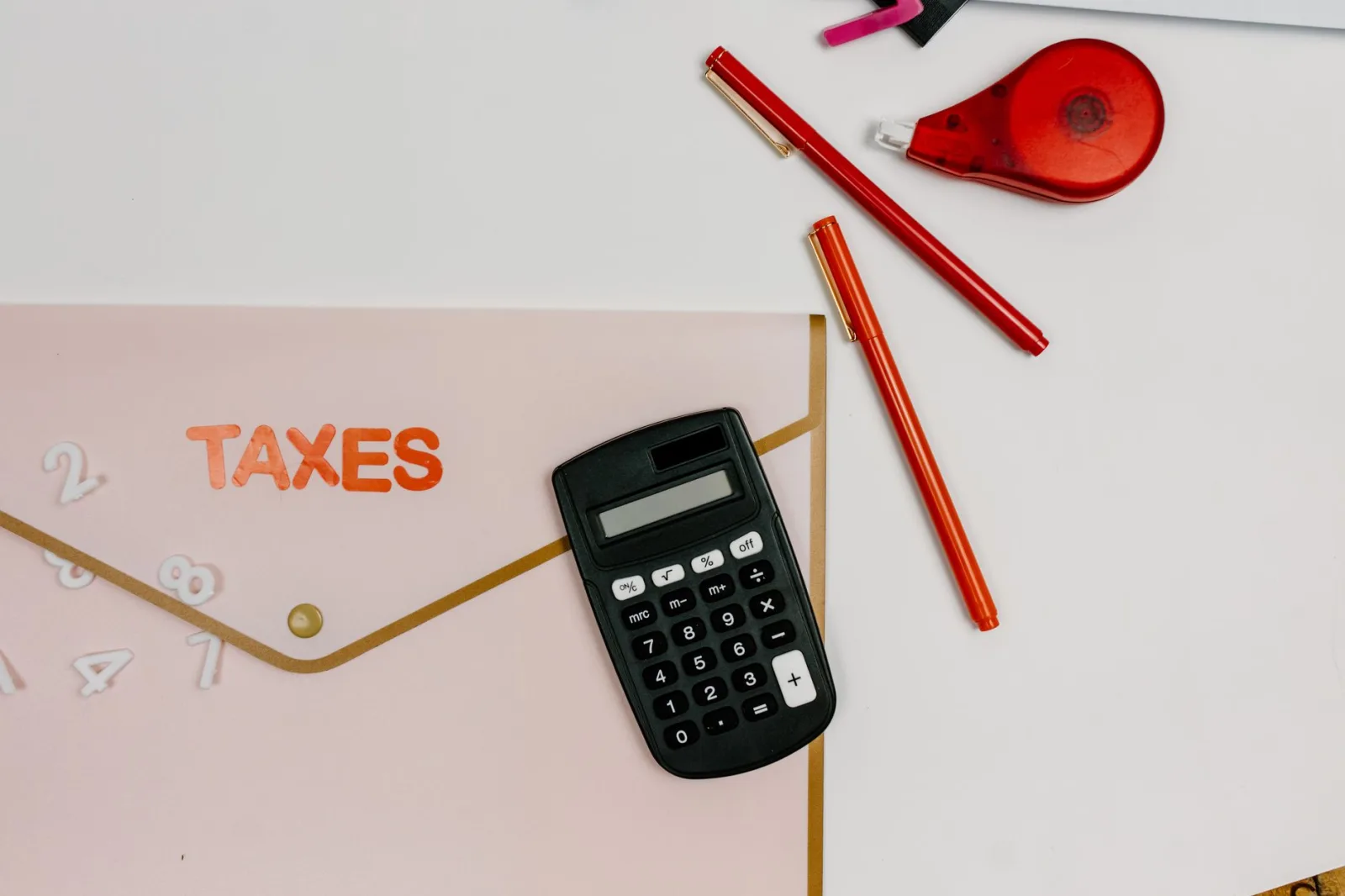 Imagen cenital de una calculadora, bolígrafos y una carpeta con la etiqueta «IMPUESTOS», ideal para temas relacionados con las finanzas.