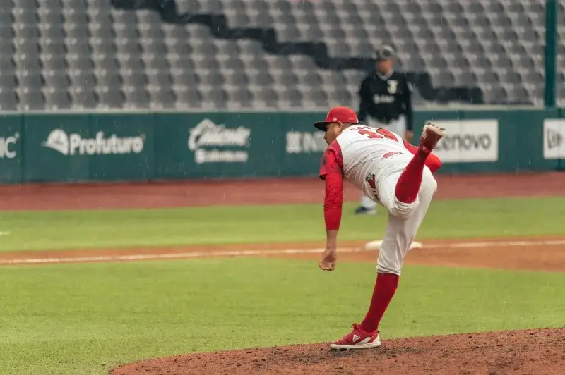 A baseball pitcher throws a pitch in a rainy stadium during a game.