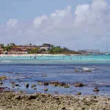 Una pintoresca escena de playa en Aruba, con aguas turquesas, una costa rocosa y animadas actividades playeras.