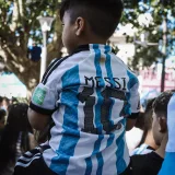 A young boy wearing a Messi jersey sits on shoulders in a festive crowd in Buenos Aires.