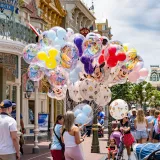 Colorful Disney-themed balloons on Main Street, USA at Disney World, with a lively crowd enjoying a sunny day.
