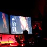 Un hombre concentrado en varias pantallas de computadora en una habitación con poca luz, que muestra un entorno de trabajo de alta tecnología.