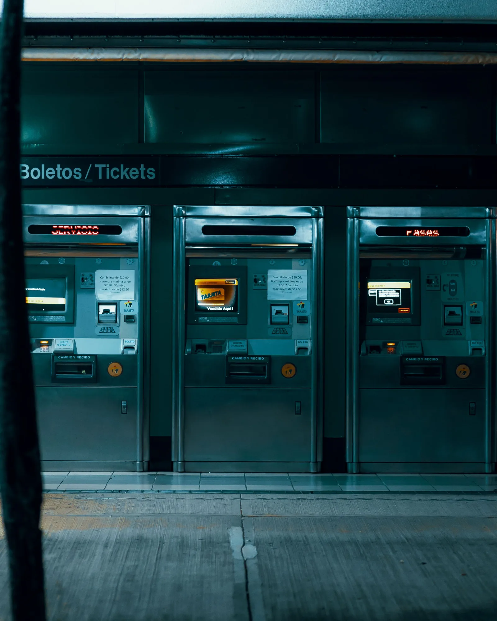 Tres máquinas expendedoras de billetes en una estación de metro tenuemente iluminada, enfatizando la tecnología urbana moderna