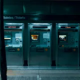 Tres máquinas expendedoras de billetes en una estación de metro tenuemente iluminada, enfatizando la tecnología urbana moderna
