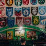 Una escena animada de un bar con logotipos coloridos de clubes de fútbol exhibidos en la pared.