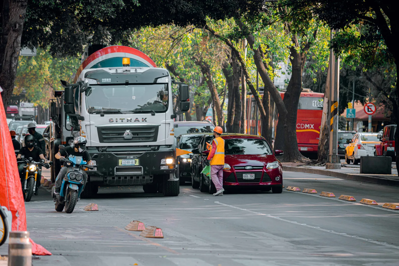 Vista de una calle con tráfico urbano, vehículos, motocicletas y un trabajador en una ciudad.