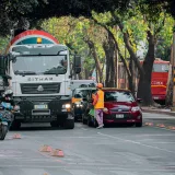 Vista de una calle con tráfico urbano, vehículos, motocicletas y un trabajador en una ciudad.