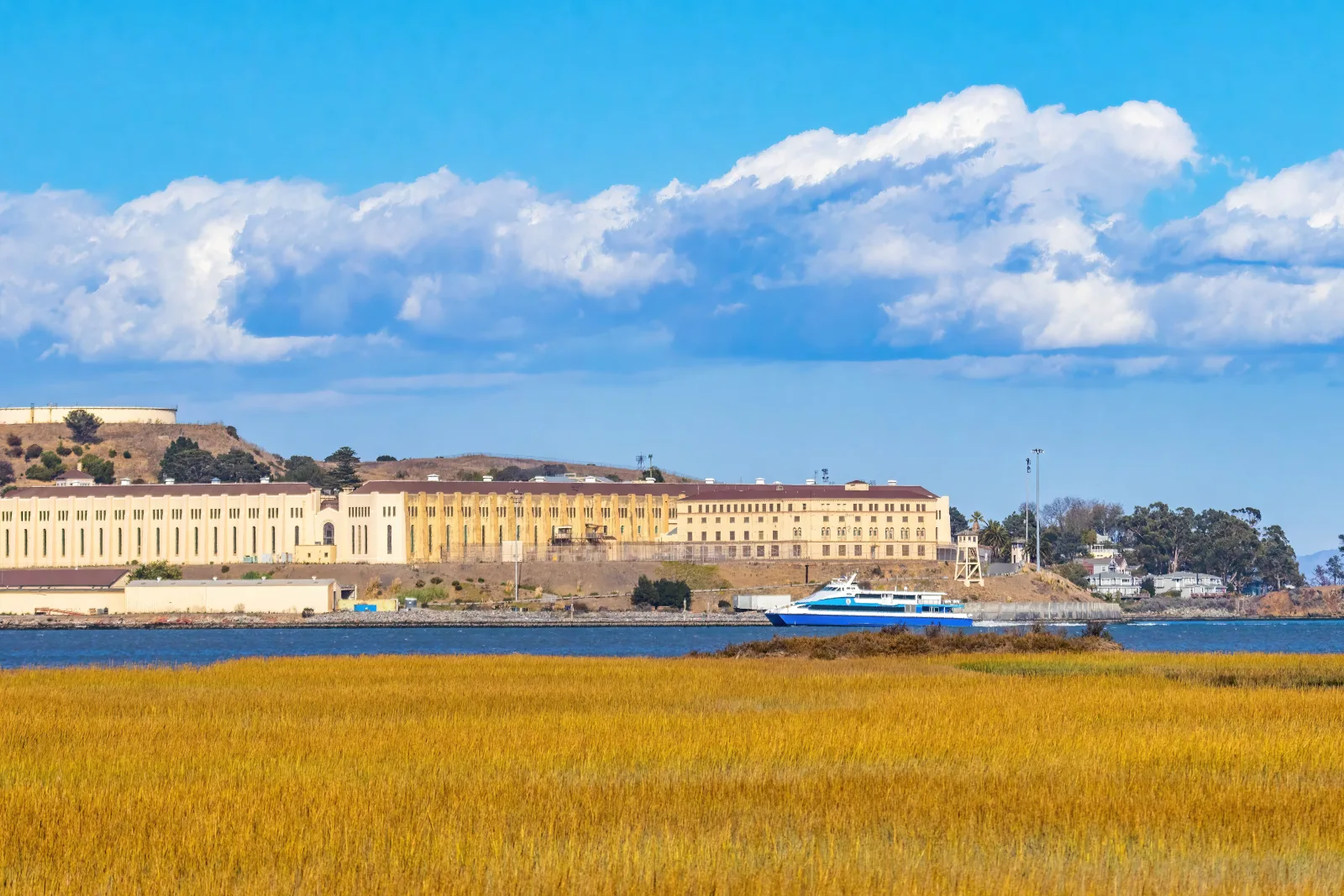 Vista de la prisión de San Quentin al otro lado del agua, con un transbordador y nubes dramáticas.