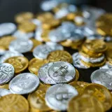 A collection of gold and silver cryptocurrency coins including Bitcoin and Ethereum on a dark surface.