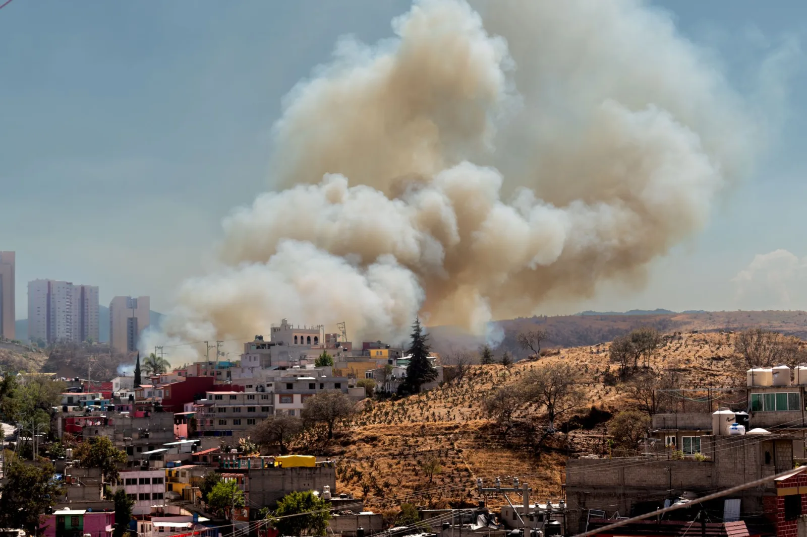 Paisaje urbano que muestra humo de un incendio detrás de edificios residenciales con el horizonte de la ciudad.