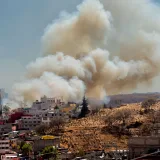 Paisaje urbano que muestra humo de un incendio detrás de edificios residenciales con el horizonte de la ciudad.