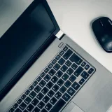 Vista de cerca de una computadora portátil plateada y un ratón inalámbrico sobre una mesa lisa, ideal para espacios de trabajo en casa.