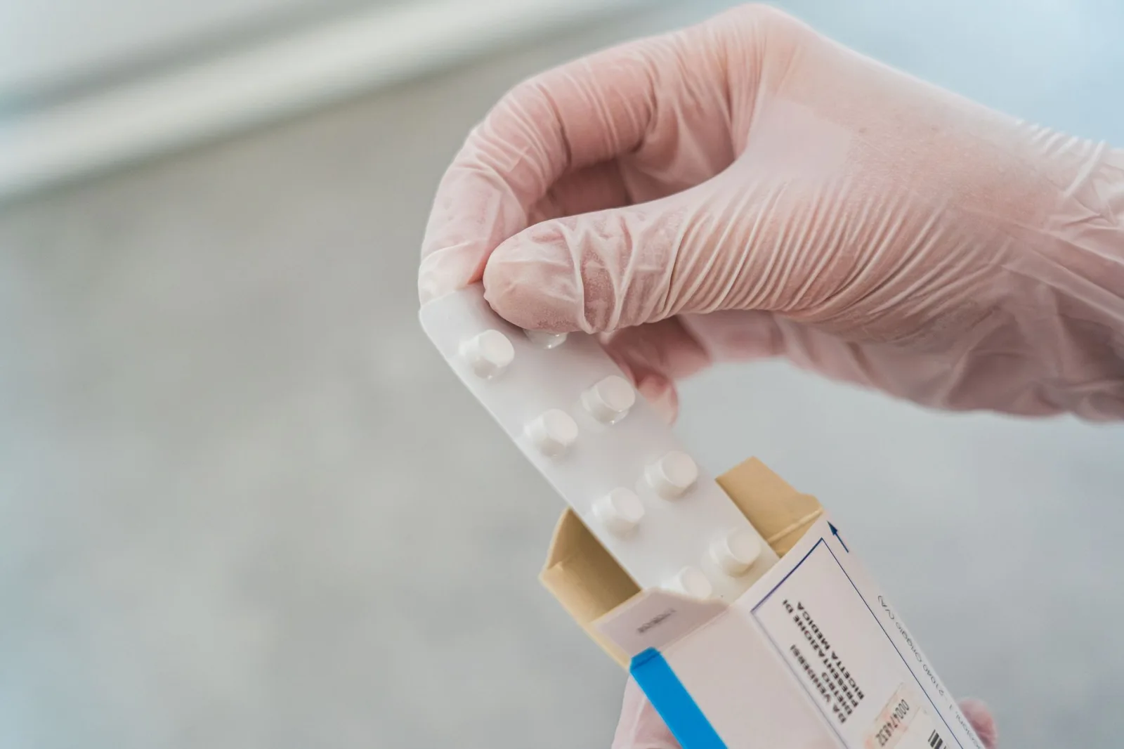 Primer plano de una mano con guantes sosteniendo un blíster de pastillas, símbolo de la atención médica.