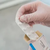 Primer plano de una mano con guantes sosteniendo un blíster de pastillas, símbolo de la atención médica.